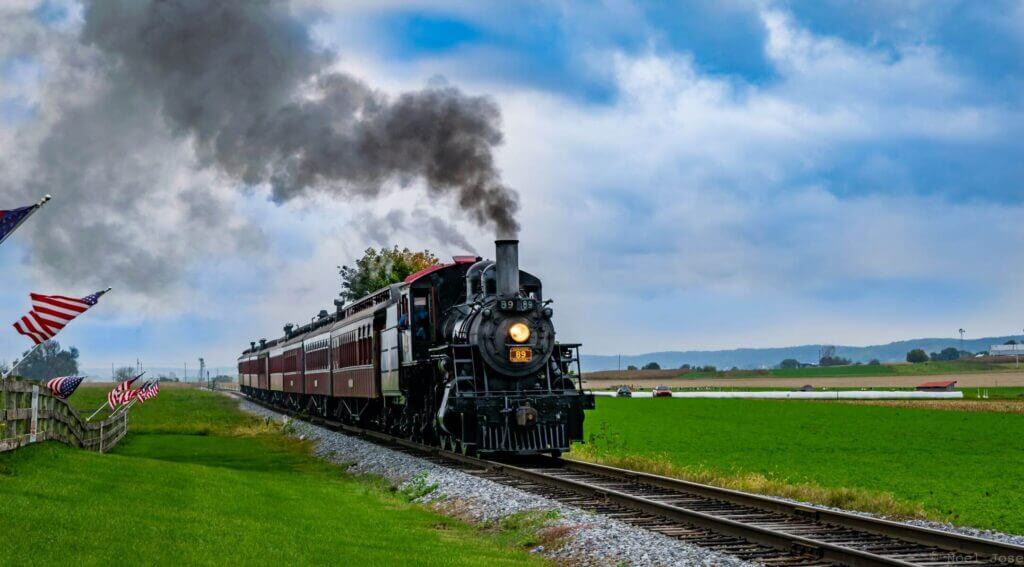 black and red running train under blue sky and green field